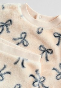 Fleece-Oberteil in Hellrosa mit dunkelblauen Schleifenmustern; verfügt über einen gerippten Kragen und eine weiche Textur für Wärme und Komfort.