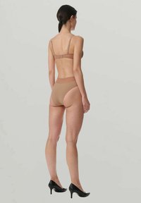 Beiger BH und passende hoch taillierte Slips, beide mit glatter Textur. Verstellbare Träger und minimalistisches Design. Getragen mit schwarzen High Heels.