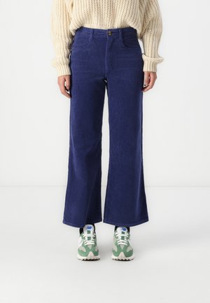 Navy corduroy wide-leg pants with front pockets and a button closure. Paired with green and white athletic shoes. Textured surface visible.