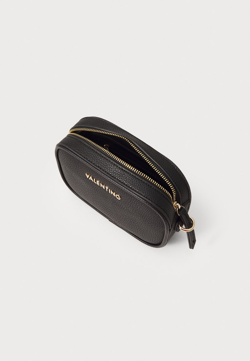 Borsa cosmetica ovale in pelle nera texturizzata con zip dorata, caratterizzata da un logo inciso sul davanti. Presenta un piccolo anello in metallo dorato.