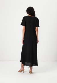 Black maxi dress with short sleeves, lace trim, and a fitted waist. Features a flowing A-line skirt and is paired with strappy nude heels.