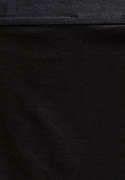 Κοντινό πλάνο μαύρου υφάσματος με μια διακριτική ραφή κοντά στην κορυφή, που αποκαλύπτει λεπτομέρειες υφής και ύφανσης.