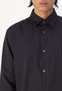 Navy button-up shirt with thin brown vertical stripes, a classic collar, and button closures. Smooth fabric with a regular fit.