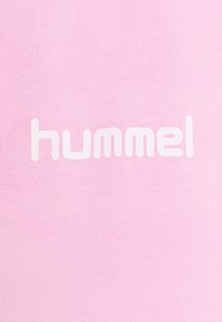 Růžová látka s žebrovanou strukturou, na které je výrazně zobrazeno bílé logo "hummel", umístěné horizontálně ve středu.