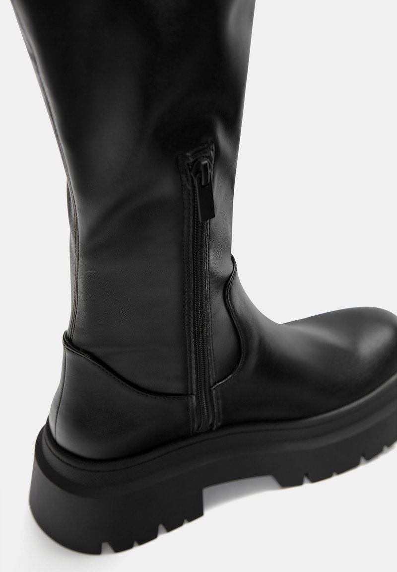 Stivale in pelle nera alto fino al ginocchio con zip laterale, punta tonda e suola in gomma spessa con profonde scanalature per una buona aderenza.