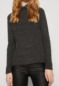 Maglione grigio lavorato a maglia con una texture a coste, caratterizzato da un collo rotondo decorato con piccole perle. Abbinato a pantaloni neri lisci.