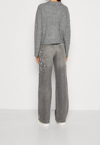 Gråstickad tröja med kort design, kombinerad med löst sittande grå jeans i denim med blekt utseende och färgstänk som detaljer.