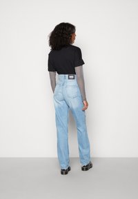 Jeans de cintura alta, azuis claros, com um corte reto, combinados com uma t-shirt preta e um top de mangas compridas em rede. Apresenta uma etiqueta da marca visível.