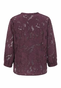 Transparante bordeaux blouse met lange mouwen, voorzien van ingewikkelde bloemige kantpatronen en een lichte textuur. Ronde halslijn met elastische manchetten.