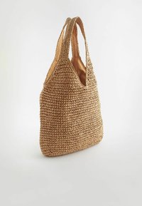 Sac fourre-tout en paille tissée couleur tan avec deux poignées, structure souple et sommet ouvert, se tenant debout sur un fond blanc.