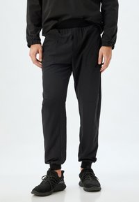 Svarta joggingsbyxor i lätt material, med elastisk midja, sidofickor och smalnande manschetter med en mjuk textur.