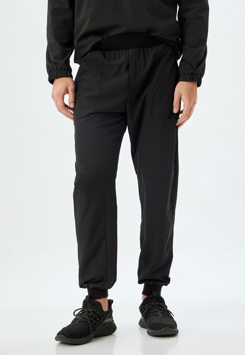 Svarta joggingsbyxor i lätt material, med elastisk midja, sidofickor och smalnande manschetter med en mjuk textur.