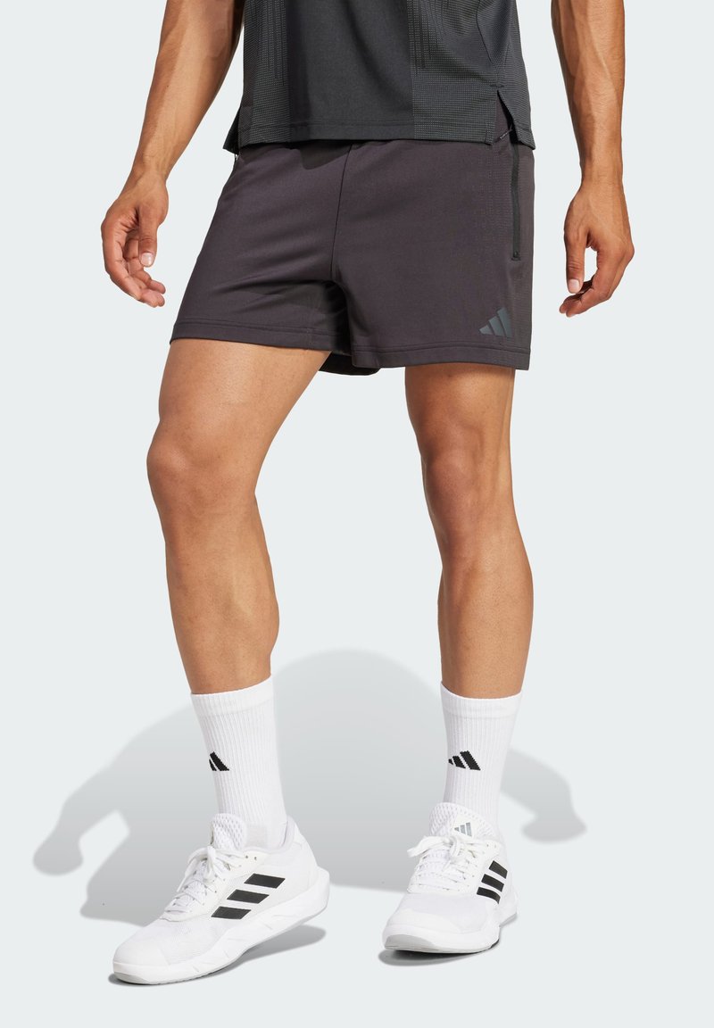 Svarte atletiske shorts laget av lett stoff, med en glidelås lomme og side-striper. Kombinert med hvite sko og sokker med svarte detaljer.