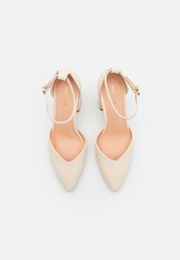 Beige-korkokengät, joissa on terävä kärki ja nilkkaremmi. Silkkinen nahkapinta, pieni korkolappu ja huomaamaton kult buckle -koristelu.