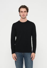 Czarny sweter z długim rękawem i okrągłym dekoltem, wykonany z miękkiej dzianiny, o dopasowanym kroju i gładkiej fakturze, zestawiony z niebieskimi dżinsami.