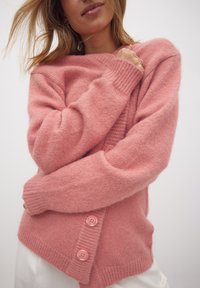 Cardigan de punto rosa, suave y con textura de pelo, con un escote en V, puños acanalados y tres botones rosas en el frente. Textura suave y un ajuste relajado.