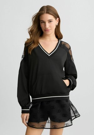 Pullover nero con scollatura a V, strisce bianche a contrasto e maniche in rete trasparente; presenta una tasca frontale e un elastico in vita.