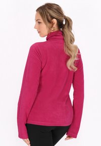 Fleece pullover magenta dengan kerah tinggi, lengan panjang, dan tekstur halus. Memiliki desain yang pas dan bahan yang lembut.