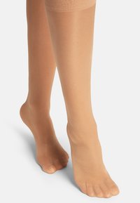 Collant trasparenti color nude con una texture liscia, design fino al ginocchio e colore naturale, che mettono in mostra i piedi con le dita esposte.