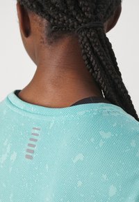 Una camiseta deportiva de color turquesa claro con un tejido texturizado y transpirable, y un detalle de franja reflectante en la parte trasera cerca del escote.