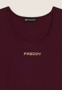 Top corto de color burdeos, hecho de algodón, con cuello redondo. Presenta un logo dorado de "FREDDY" en el frontal, textura suave y diseño casual.