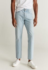 Jeans de denim azul claro con corte recto, que cuentan con cinco bolsillos y un cierre de botón, combinados con zapatillas blancas y una camiseta básica.