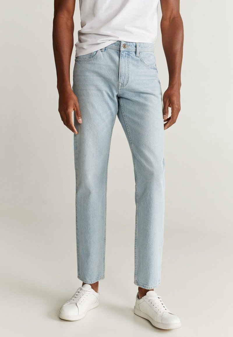 Jeans de denim azul claro con corte recto, que cuentan con cinco bolsillos y un cierre de botón, combinados con zapatillas blancas y una camiseta básica.