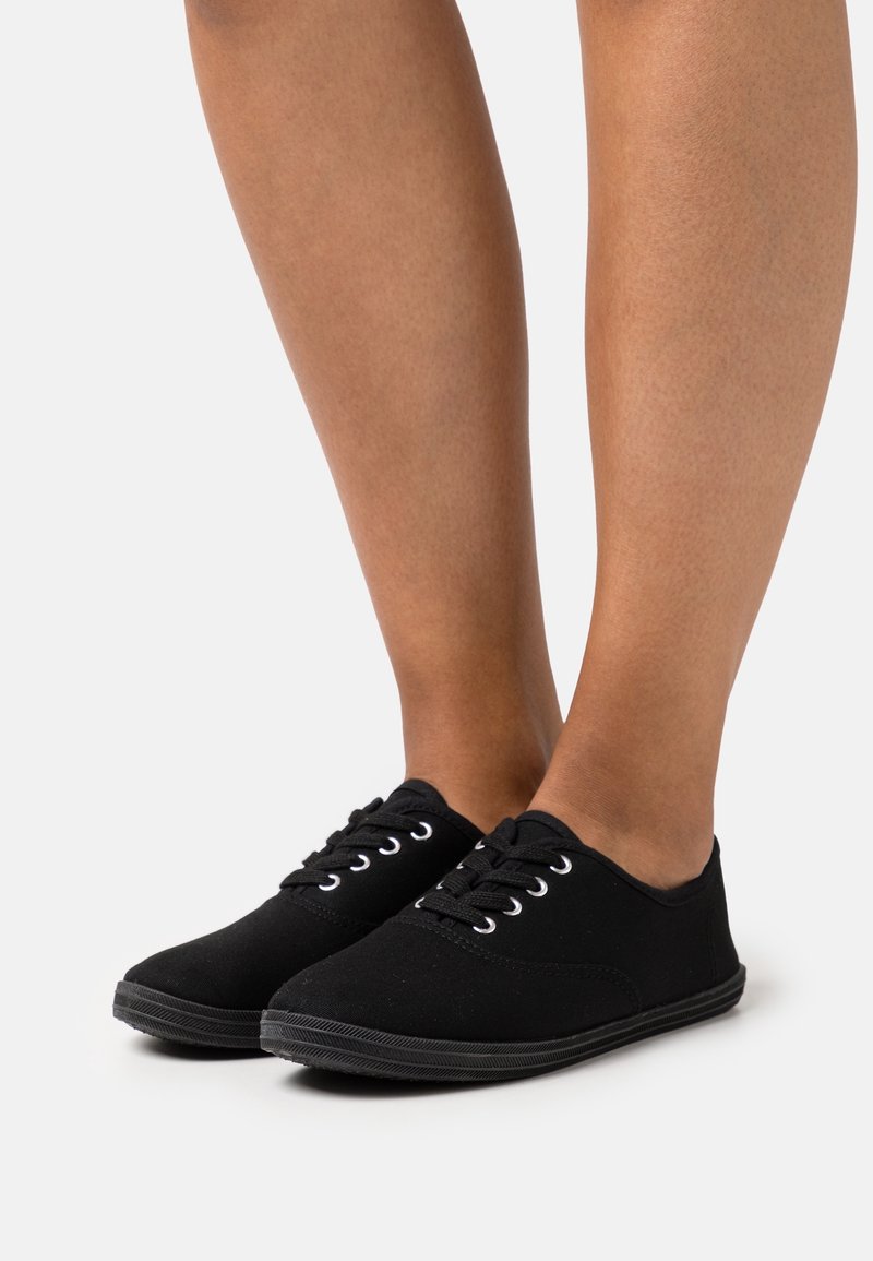 Czarne sneakersy na płaskiej podeszwie, z białymi oczkami i czarnymi sznurówkami. Teksturowana gumowa podeszwa zapewniająca przyczepność i trwałość.