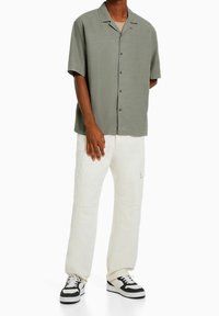 Koszulka z krótkim rękawem, zapinana na guziki w oliwkowym kolorze; w połączeniu z off-white spodniami cargo z bocznymi kieszeniami i ciemnymi trampkami.