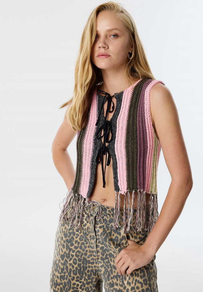 Dzianinowy top w fasonie crop z naprzemiennymi różowymi, zielonymi i czarnymi paskami, z przodem na sznurki i frędzlami na dolnym końcu. Noszony na legginsach w panterkę.