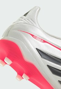 Chaussure de football blanche avec une tige texturée, des accents noirs et une semelle extérieure rose vif. Présente un logo "Copa" et un design avec talon surélevé.