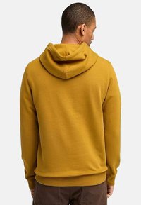 Haut à capuche jaune moutarde avec cordon de serrage, poignets côtelés et ourlet. Texture lisse sans motifs visibles ni détails en métal.