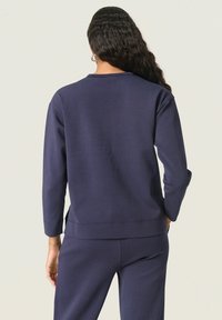 Sudadera azul marino con mangas largas y cuello redondo, con una textura suave y aberturas laterales para facilitar el movimiento.