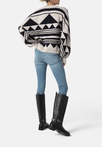 Maglione lavorato a maglia con motivo geometrico in crema e blu navy, abbinato a jeans skinny azzurri e stivali al ginocchio in pelle nera.
