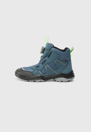 Botte de randonnée bleue avec tige en synthétique, capot de protège-orteil en caoutchouc noir, mécanisme de laçage rapide ajustable et accent vert sur le talon.