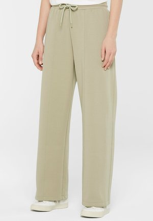 Beige Hosen mit weitem Bein, Frontnähten und einem Tunnelzugbund, kombiniert mit weißen Sneakers und einem weißen Oberteil.