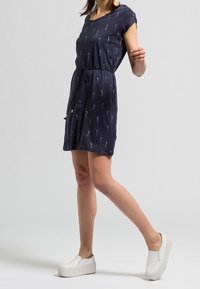 Granatowa sukienka z krótkim rękawem w strzałkowy wzór, zaciśnięta w talii sznurkiem, połączona z białymi platformowymi butami typu slip-on.