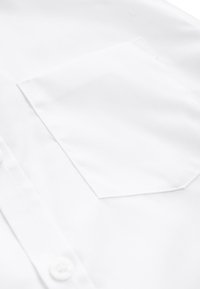 Gros plan sur le tissu d'une chemise blanche montrant une poche poitrine avant et des boutons blancs le long du plastron.