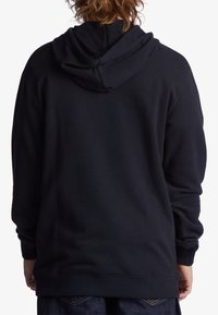 Sudadera negra con capucha ajustable, fabricada en un tejido suave y texturizado, con puños acanalados y un corte relajado. Sin logotipos ni patrones visibles.