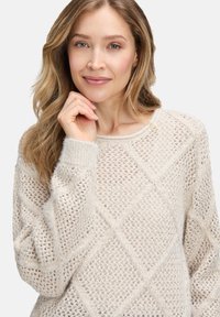Hellbeige Strickpullover mit einem Diamantmuster, langen Ärmeln und gerippten Bündchen. Aus weichem, strukturiertem Material in lockerer Passform gefertigt.