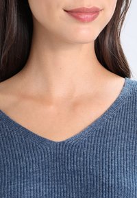 Top in maglia a coste blu con scollatura a V, caratterizzato da una texture morbida e una vestibilità aderente attorno al collo e alle spalle.