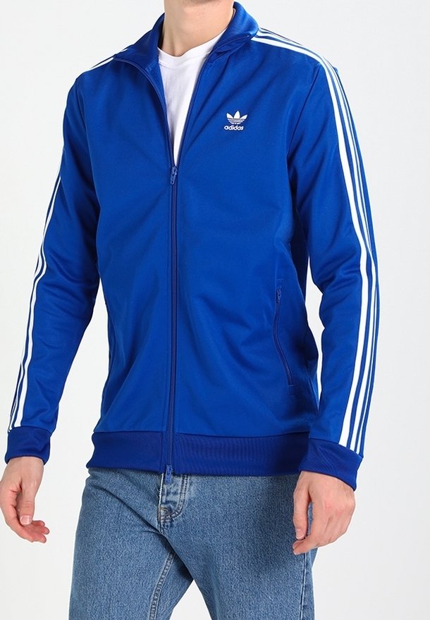 Blauwe ritssluitingjack met witte strepen op de mouwen. Heeft een hoge kraag, zacht materiaal, geribbelde manchetten en een Adidas-logo op de borst.