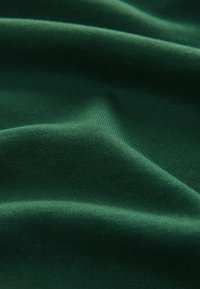 Tela verde oscuro con una textura suave, que muestra una ligera elasticidad y un caído suave. La superficie tiene un patrón de punto consistente y un color uniforme.