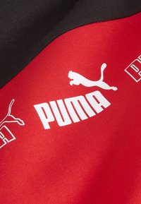 Tessuto rosso e nero con il logo Puma e lettering bianchi in evidenza, texture liscia e contrasto di colori distintivo.