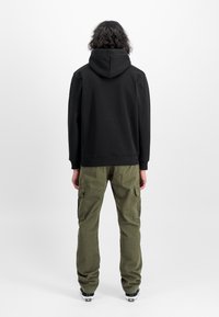 Felpa nera con cappuccio e pantaloni cargo verde oliva. La felpa ha una vestibilità comoda; i pantaloni sono dotati di tasche laterali e gambe affusolate.