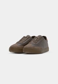 Brown sneakers featuring a suede and synthetic material mix, round toe, flat laces, and textured rubber sole with a zigzag pattern.