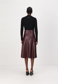 Haut noir à manches longues côtelé associé à une jupe midi en cuir bordeaux, avec une taille ajustée et un ourlet évasé, vu de dos.