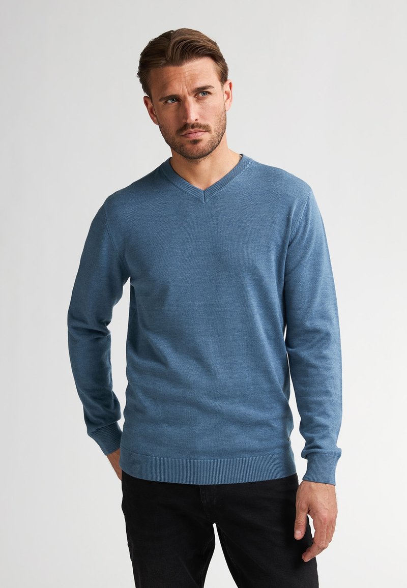 Pulover cu decolteu în V, de culoare albastru deschis, din material tricotat, cu mâneci lungi, cu manșete și tiv cu dantelă, design ajustat. Purtați-l cu pantaloni negri.