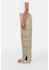 Licht khaki cargobroek met meerdere zakken, relaxte pasvorm, zijsplitten aan de onderrand, gemaakt van een zachte stof, gecombineerd met witte hak sandalen.