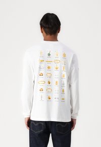 Langærmet hvid t-shirt med et grafisk print af guld dekorative genstande på ryggen, herunder kæder, cannabis blade og dollarskilt.